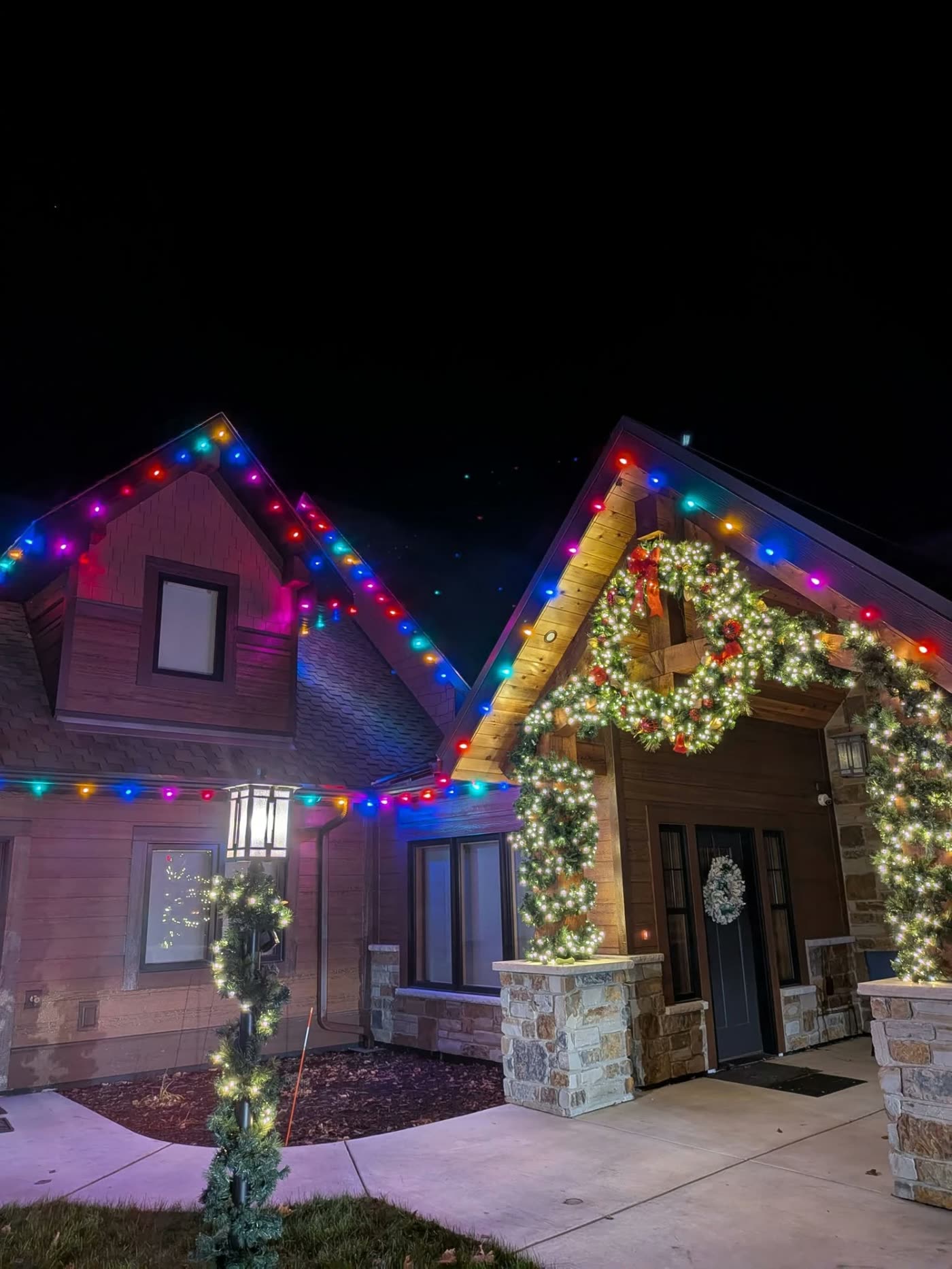 Craftsman entry with multicolor roofline lights and lit garland arches